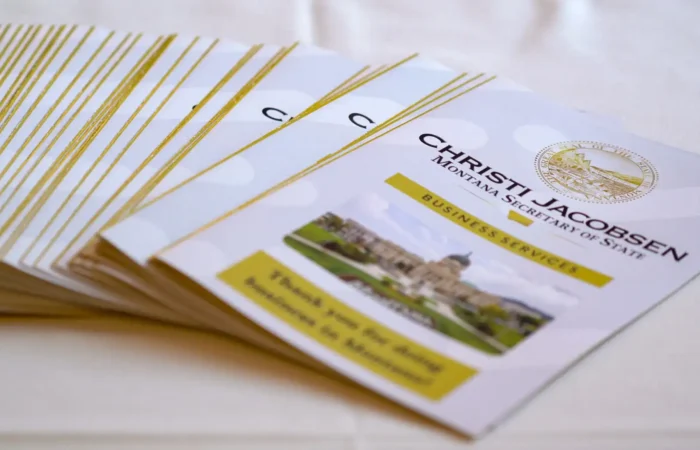 More than 50,000 annual reports filed with the Montana Secretary of State's Office to date 10 A stack of brochures titled “Christi Jacobsen Montana Secretary of State Business Services,” featuring a seal and a photo of the Montana State Capitol on the front, arranged neatly on a white tablecloth.