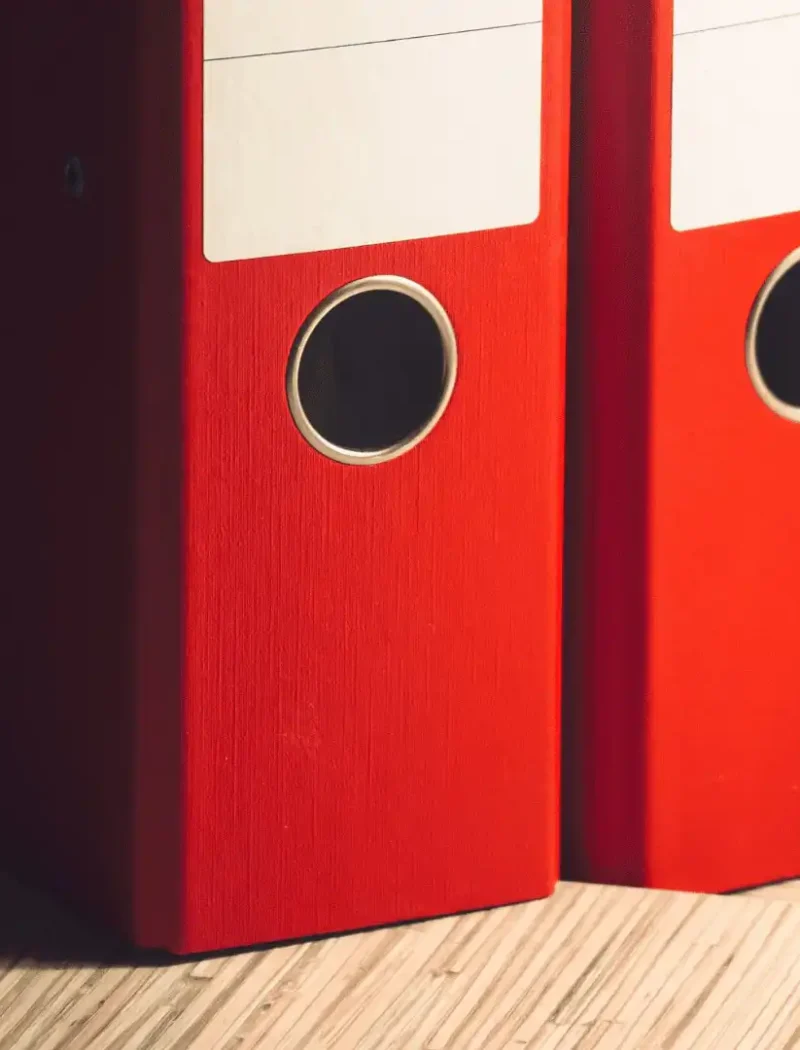 Two red file binders stand upright on a wooden surface, with the text Montana Candidate Filing to the left—signaling the start of candidate filings ahead of opening weekend.