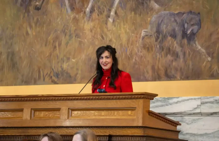 Secretary Christi Jacobsen: 'More than 6,000 new businesses registered in January 2025' 2 Secretary of State Christi Jacobsen, wearing a red blouse, stands at a wooden podium with microphones, smiling in front of a mural featuring animals and tall grass during the 69th Legislative Assembly.