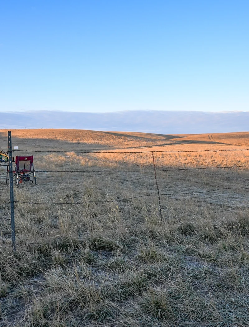 Secretary Christi Jacobsen votes to advance plans for a public shooting range for Gallatin Valley hunters and shooters 1 A folding chair and small table with a rifle sit behind a fence at the site of the proposed Logan Public Shooting Range in the Gallatin Valley, with a State Trust Land sign visible in the background.