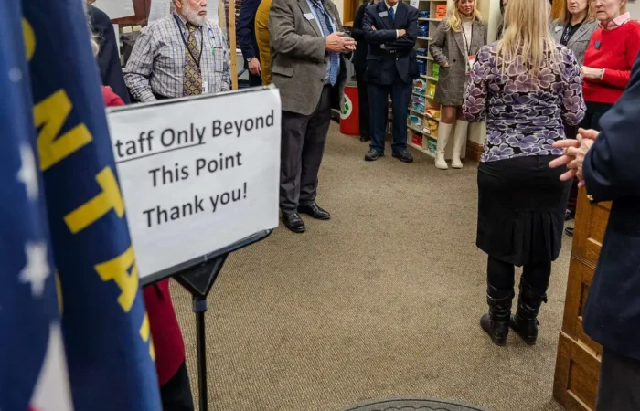 SOS Office joins House State Administration in visit of Lewis and Clark County Elections Office 3 A group of people stand and talk beyond a sign that reads Staff Only Beyond This Point Thank you! An American flag is visible in the foreground, and the setting appears to be indoors, possibly a library or office.