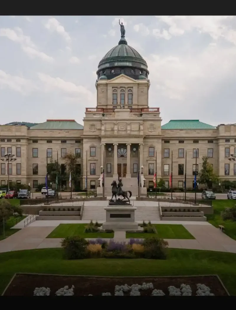 A large, domed government building with columns and a statue in front, surrounded by green lawns, trees, and parked cars—a distinctive scene from 2021 as new Montana businesses emerged against hills and a cloudy sky backdrop.