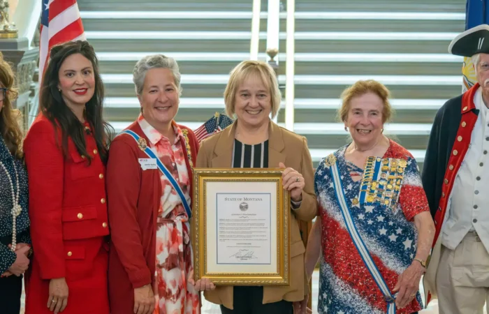 Secretary Christi Jacobsen launches 2024 U.S. Constitution Contest for all Montana students 1 Six people stand smiling in front of a staircase; the central person holds a framed certificate. Two women wear patriotic-themed dresses, one man wears a colonial outfit, and others are in red attire. Montana students celebrate the U.S. Constitution Contest.