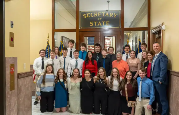 Secretary Christi Jacobsen welcomes several Class C, homeschool students to Montana State Capitol 6 A group of young adults, including some homeschool students and adults, pose together for a photo in front of the Secretary of State office entrance inside the Montana State Capitol. Most are dressed formally and smiling at the camera.