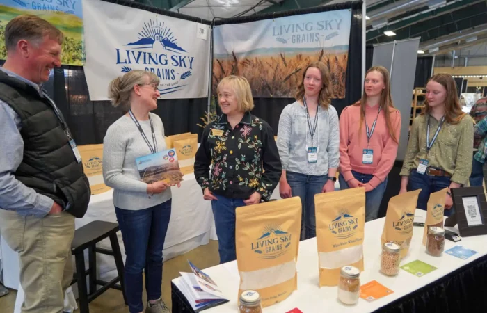VIDEO: Secretary Jacobsen congratulates businesses honored at 2024 Made in Montana Tradeshow 1 Five people stand and smile at a booth for Living Sky Grains, with various grain products displayed on the table in front of them at what appears to be an indoor market or trade show.