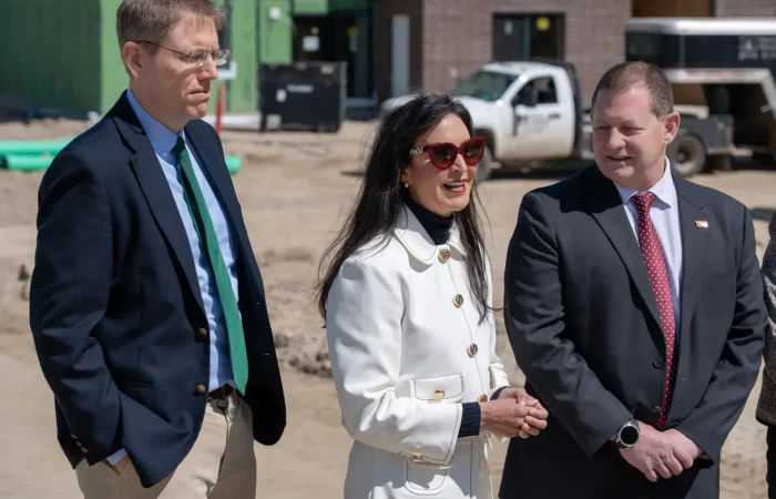 Secretary Christi Jacobsen: 'Record number of new business registrations in April 2025' 6 Secretary Christi Jacobsen stands at a construction site in April 2025 with two colleagues, highlighting the surge in new business registrations. The woman wears a white coat and sunglasses, flanked by two men in suits, with vehicles and materials in the background.