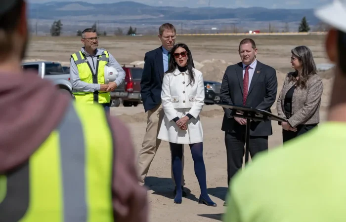 Secretary Christi Jacobsen joins Governor, Legislators to celebrate historic tax cut for Montana businesses 3 Secretary Christi Jacobsen addresses the crowd at a podium outdoors, flanked by officials. People in high-visibility vests stand nearby, while construction vehicles and Montana businesses are set against a mountainous backdrop.