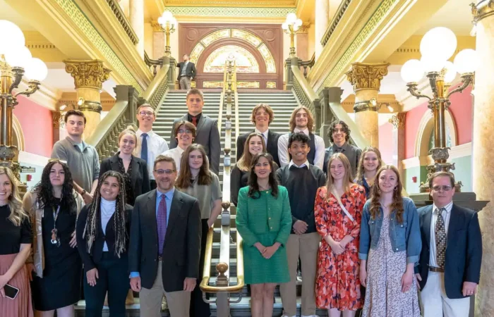 Secretary Christi Jacobsen visits with students from Stevensville High School 2 A group of people, including students from Stevensville High School and several adults, stand posing for a photo on a grand staircase inside a historic building with ornate columns, decorative lights, and colorful walls.