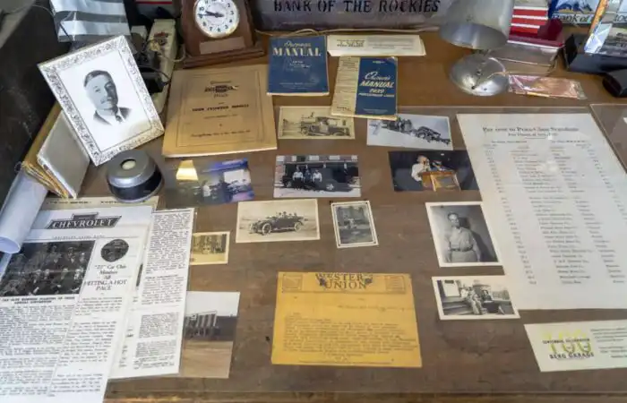 Montana Business Spotlight: Berg Garage proud to ‘take care of the people’ in Meagher County 6 A wooden desk displays old photographs, documents, newspapers, a clock, vintage car manuals from Berg Garage, a framed black-and-white portrait, and a yellow Western Union telegram, creating a nostalgic Meagher County historical scene.