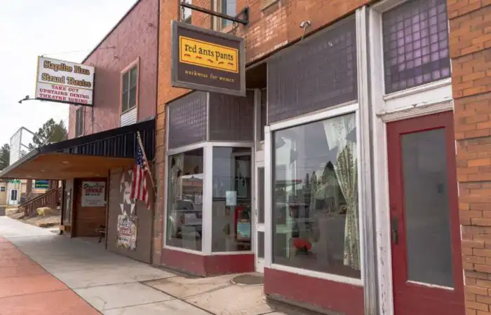 Montana Business Spotlight: ‘Fun to see what’s possible’ with Red Ants Pants 5 Street view of small-town brick storefronts, including Red Ants Pants—a Montana Business with a yellow sign and large windows—and a theater marquee displaying an American flag, all lining a quiet sidewalk.