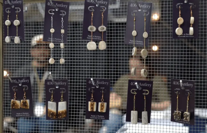 Montana Business Spotlight: 406 Antlery crafts one-of-a-kind, handmade creations 6 A display of handmade earrings by 406 Antlery, a Montana business, arranged on a mesh screen. Each rustic pair is attached to branded cards while blurred figures sit in the background, highlighting the unique handmade creations.
