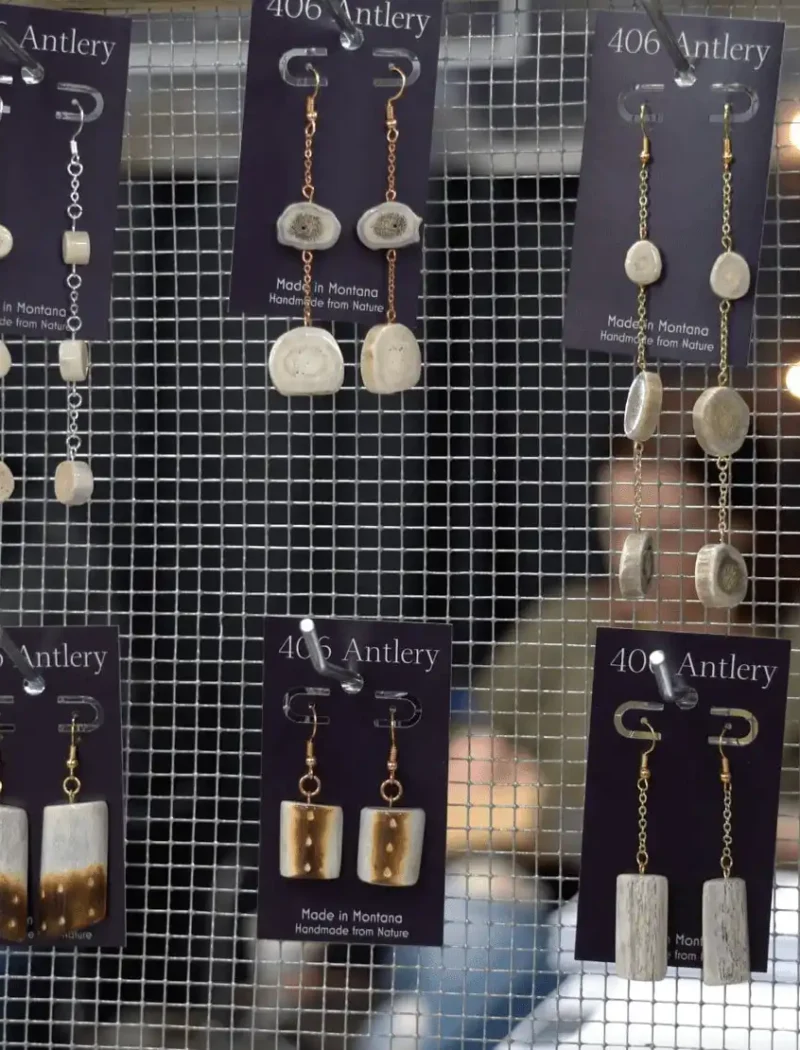 Montana Business Spotlight: 406 Antlery crafts one-of-a-kind, handmade creations 8 A display of handmade earrings by 406 Antlery, a Montana business, arranged on a mesh screen. Each rustic pair is attached to branded cards while blurred figures sit in the background, highlighting the unique handmade creations.