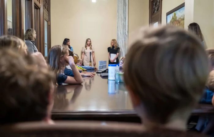 Secretary Christi Jacobsen visits with Smith Elementary students at Montana State Capitol 1 A group of children from Smith Elementary sit around a large table in a conference room at the Montana State Capitol, listening to Secretary Christi Jacobsen and two other women at the front. The atmosphere appears educational or formal.