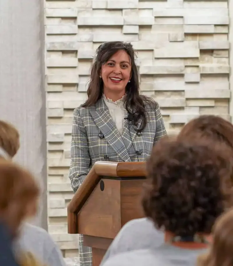 Secretary of State Christi Jacobsen stands at a podium, smiling as she addresses the 2022 American Legion Boys State attendees. Behind her, the National Guard emblem is displayed while the audience listens attentively.