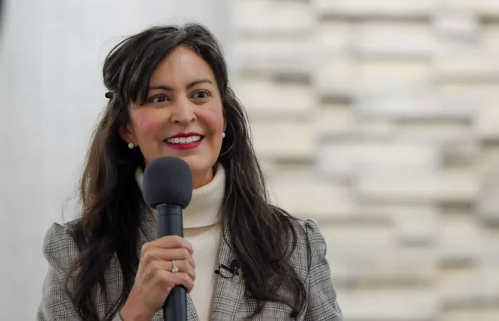 Secretary of State Christi Jacobsen waiving 2025 Annual Report fees, again saving Montana businesses millions 8 A woman with long dark hair, wearing a plaid blazer and turtleneck, smiles while speaking into a microphone. In the background, a blurred stone wall and part of a round sign hint at Montana businesses and 2025 Annual Report fees discussion.