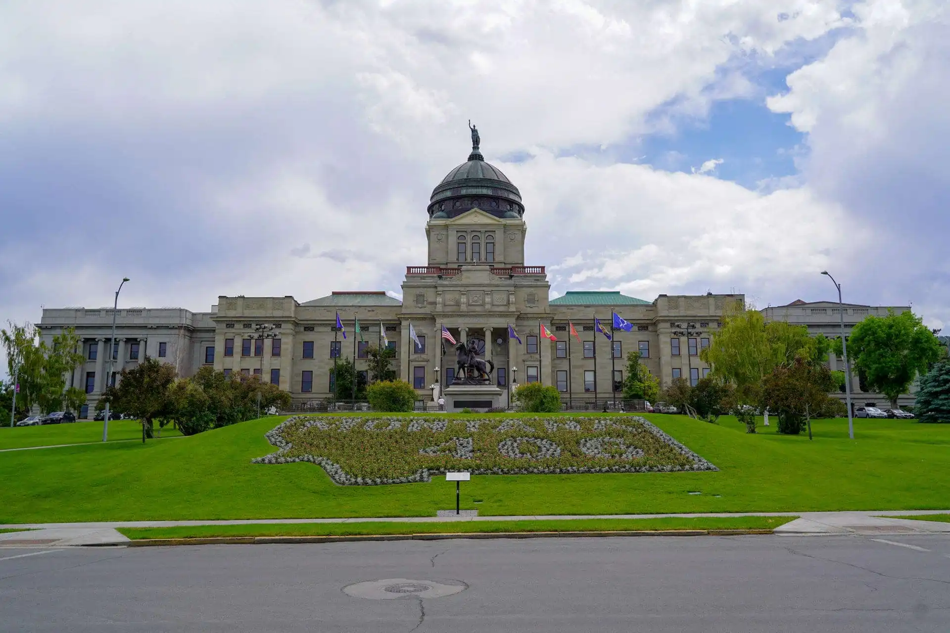 Board of State Canvassers completes State Canvass for 2022 Primary Election 20 The Montana State Capitol building with its domed roof stands proudly amid green lawns and state flags, while a floral design graces the grass in front—capturing the spirit reflected during the 2022 Primary Election.