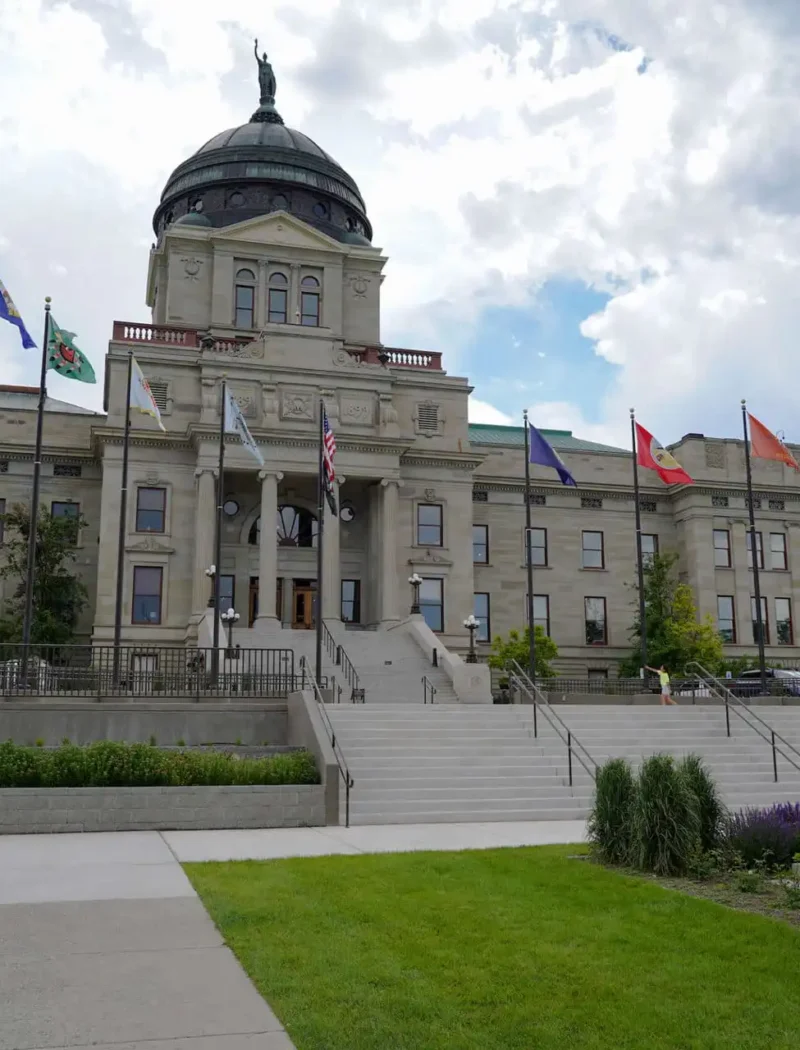 Secretary Christi Jacobsen announces August’s new business registrations 3 The image shows the Montana State Capitol building with its large dome, surrounded by flags and a statue of a person on horseback in the foreground—a place where Secretary Christi Jacobsen oversees new business registrations. The sky is partly cloudy.