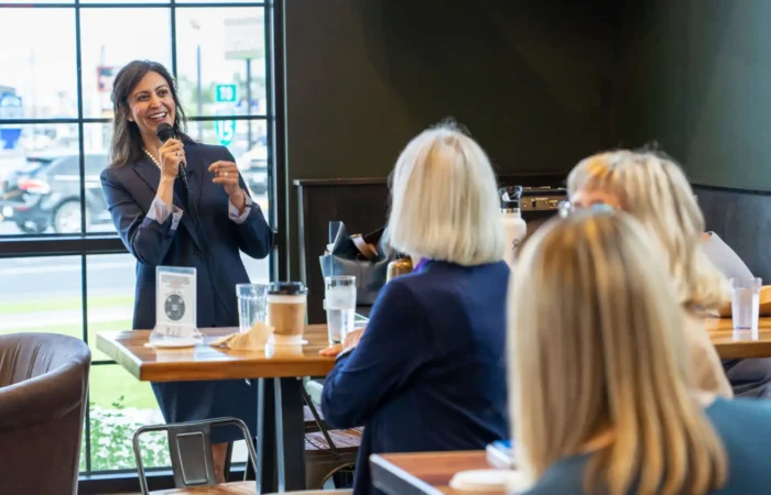 Secretary Christi Jacobsen grateful for 2022 successes 7 Secretary of State Christi Jacobsen smiles as she speaks into a microphone, addressing the Helena Rotary and a group of seated women in a bright, modern cafe with large windows.
