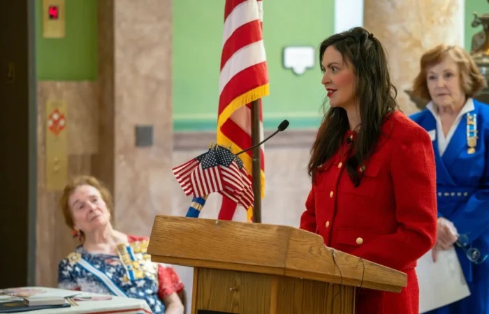 Secretary Christi Jacobsen: 'New business registrations climbed again in November 2024' 4 Christi Jacobsen, in a red coat, speaks at a podium decorated with small American flags during a Constitution Day celebration. An elderly woman sits beside her, while another woman in blue stands near an American flag in the background.