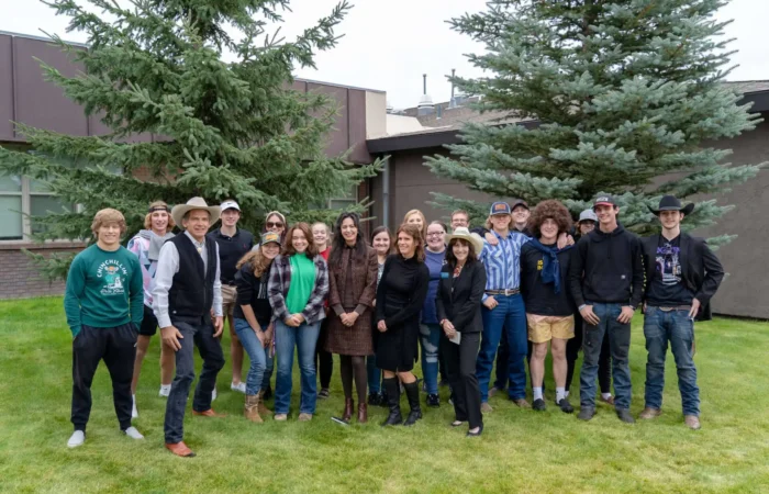 Secretary Christi Jacobsen talks upcoming election, business growth during visit to Boulder 10 A group of people, mostly young adults and a few adults, stand smiling together on grass in front of a building and pine trees. Many wear casual clothes, some have hats, and the setting appears outdoors during an event about the upcoming election.