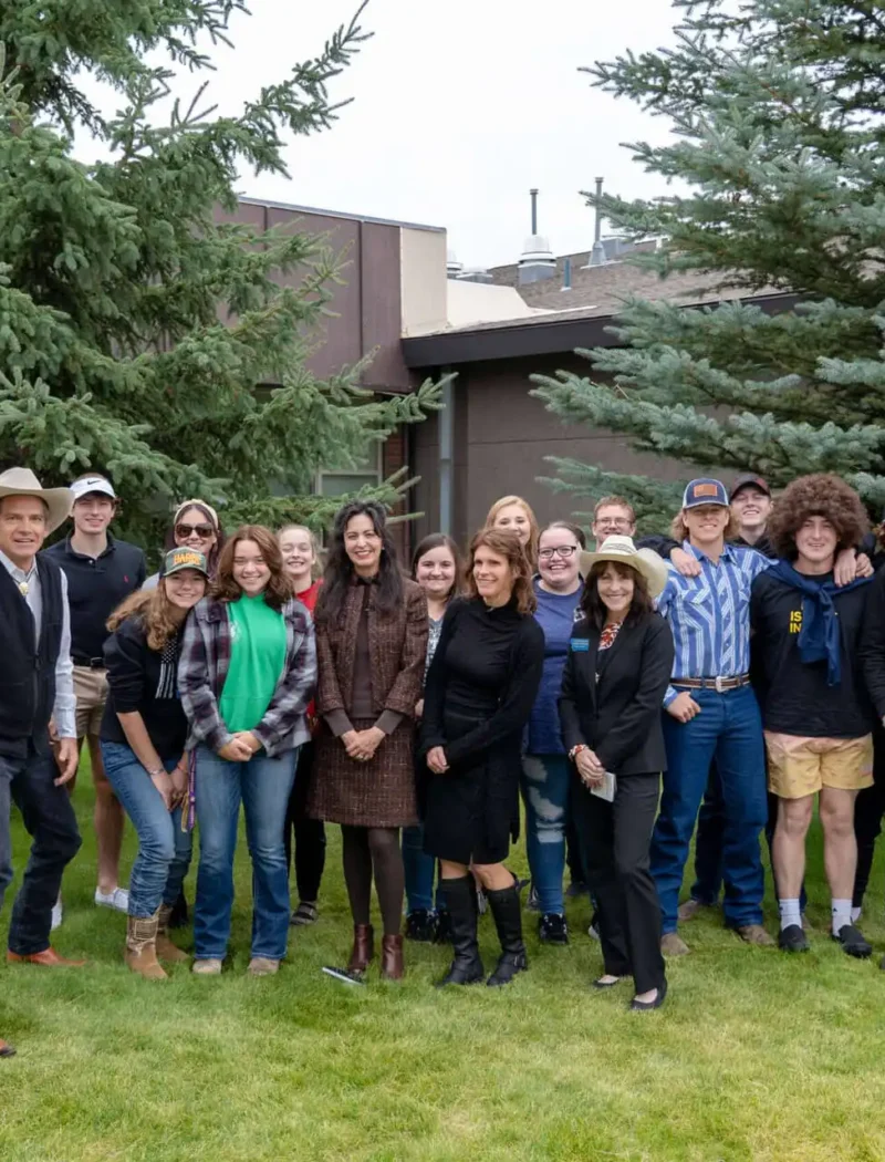 Secretary Christi Jacobsen talks upcoming election, business growth during visit to Boulder 2 A group of people, mostly young adults and a few adults, stand smiling together on grass in front of a building and pine trees. Many wear casual clothes, some have hats, and the setting appears outdoors during an event about the upcoming election.