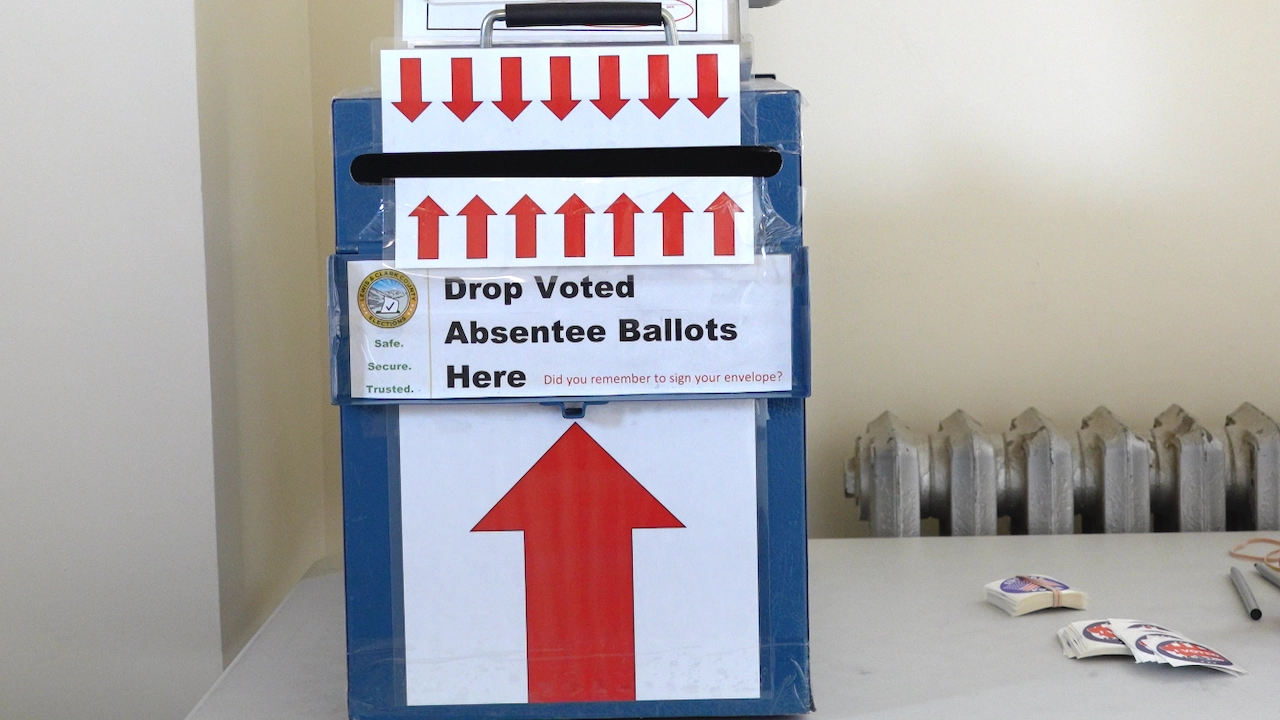 A blue Montana absentee ballot drop box with a sign that reads Drop Voted Absentee Ballots Here and a large upward-pointing arrow.