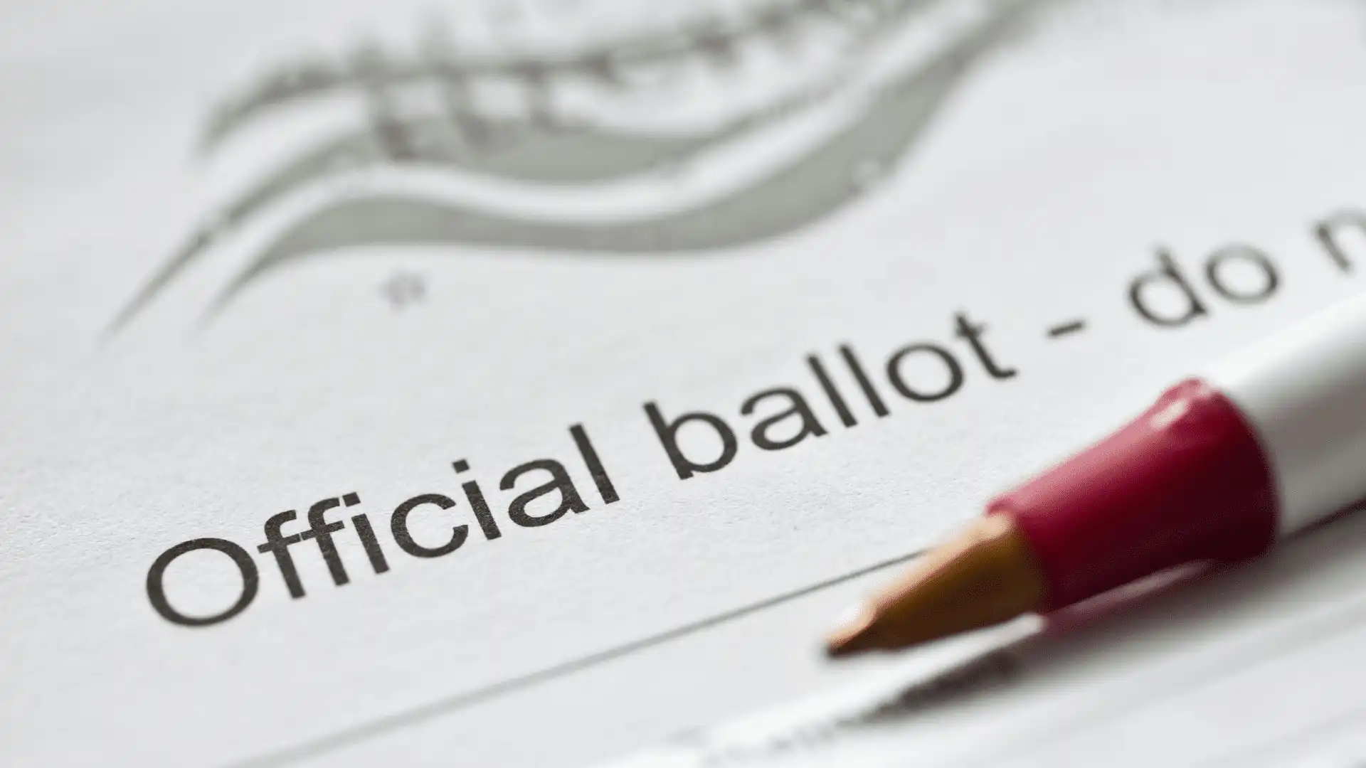 A close-up of an official ballot paper with the words Official ballot clearly visible. A red and white pen rests on the paper, suggesting someone is about to fill it out as Montana Secretary of State Christi Jacobsen certifies candidates.