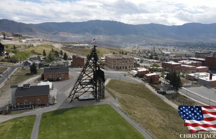 Secretary of State Christi Jacobsen joins Montanans in celebrating #America250 3 Aerial view of historic mining town in Butte with old mine structures, brick buildings, open grassy areas, and mountains in the background. An American flag, America250, and Secretary of State Christi Jacobsen appear in the bottom right corner.