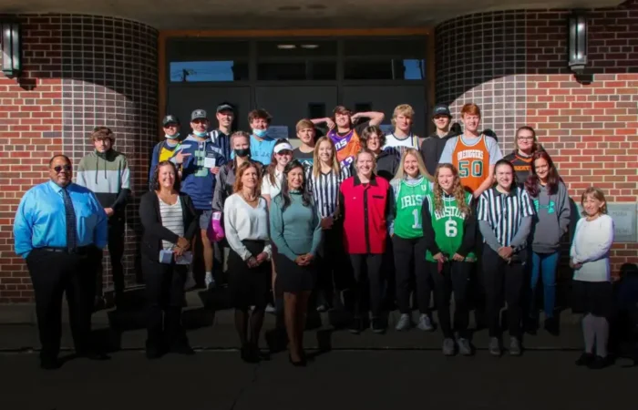 Secretary Jacobsen delivers Constitutions to Butte Central students 8 A group of Butte Central students and adults pose together outside a brick building. Some are wearing sports jerseys or referee shirts, and all are smiling in the sunlight.