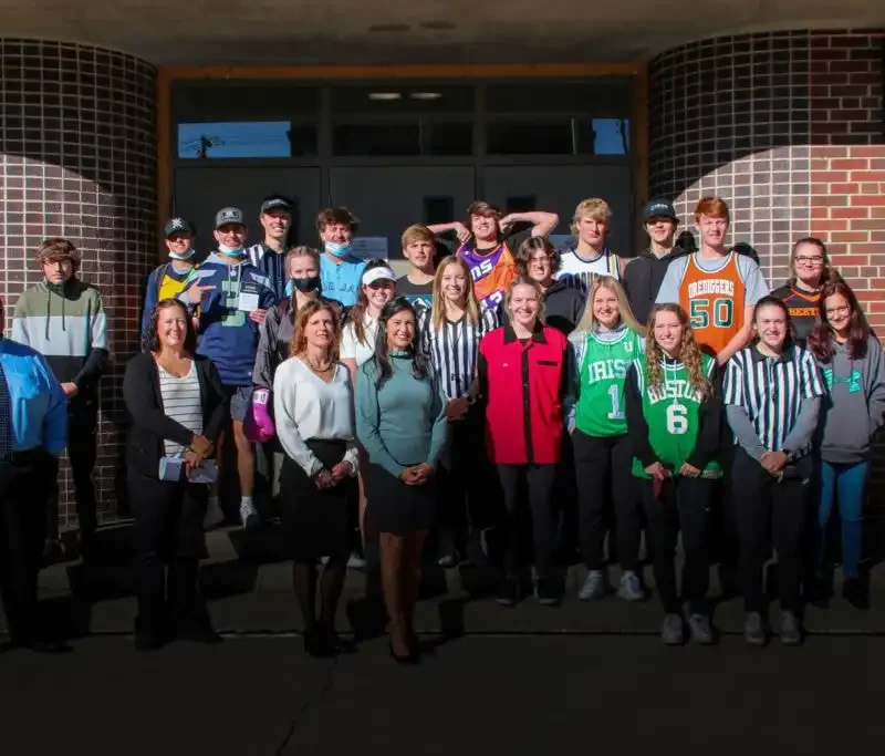 Secretary Jacobsen delivers Constitutions to Butte Central students 8 A group of Butte Central students and adults pose together outside a brick building. Some are wearing sports jerseys or referee shirts, and all are smiling in the sunlight.