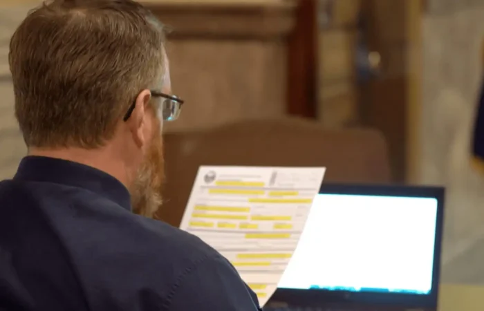 Secretary of State's Office reports 32 new candidate filings this week 2 A man with glasses and a beard sits at a desk, reading highlighted candidate filings. An open laptop glows in front of him as he reviews new candidate forms, likely related to the Secretary of State, in an indoor formal setting.