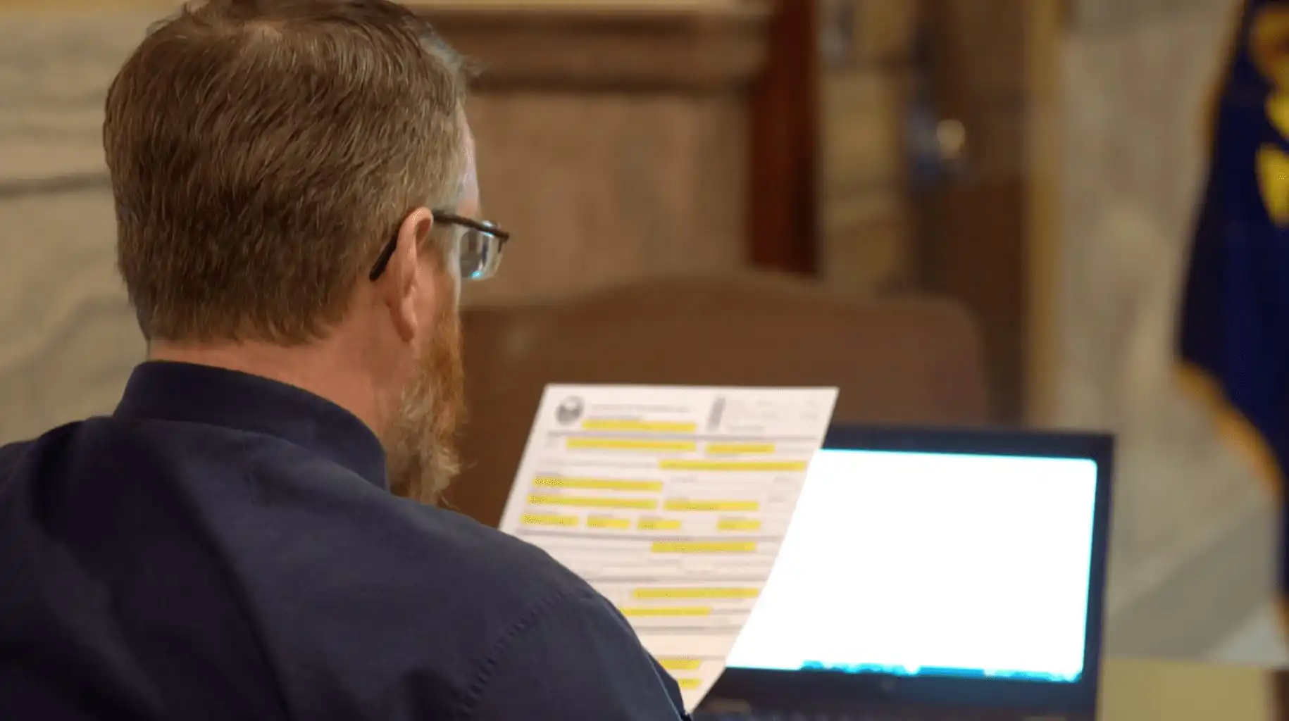 Secretary of State's Office reports 32 new candidate filings this week 16 A man with glasses and a beard sits at a desk, reading highlighted candidate filings. An open laptop glows in front of him as he reviews new candidate forms, likely related to the Secretary of State, in an indoor formal setting.