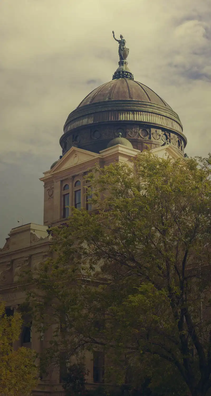 A domed classical building, partially obscured by leafy trees and a cloudy sky, features ornate architecture and a statue holding an object&mdash;reminiscent of the careful organization of an office file.