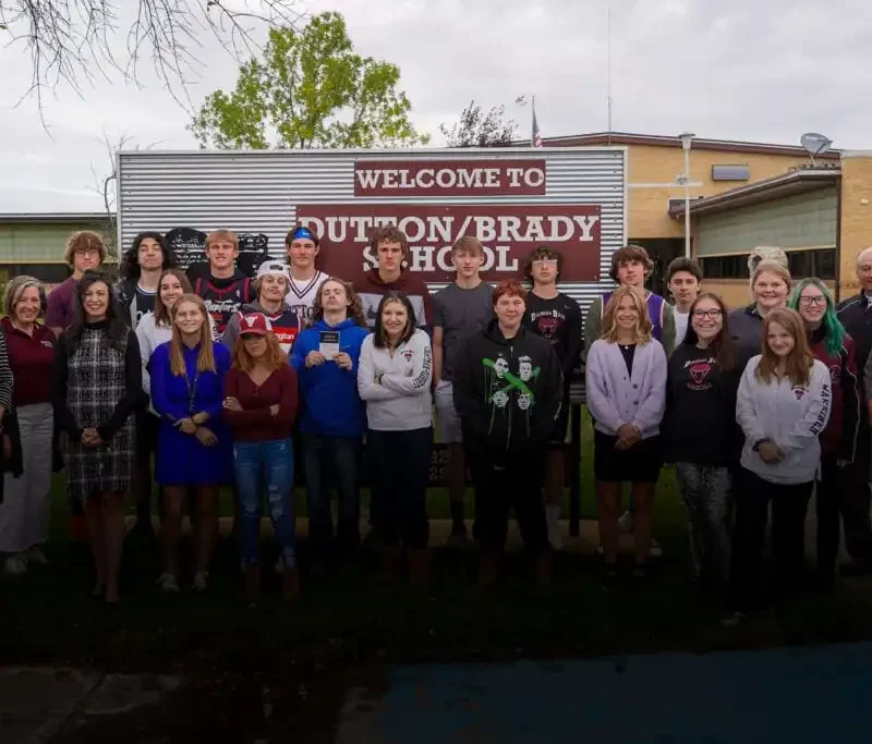 Secretary Jacobsen visits Dutton-Brady Schools, delivers Constitutions 7 A group of students and adults pose together in front of Dutton-Brady Schools, where Secretary Jacobsen delivers Constitutions. They stand on grass under a cloudy sky by a sign that reads Welcome to Dutton/Brady School.