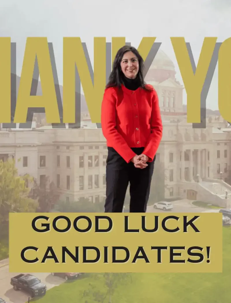 Secretary Christi Jacobsen stands in a red jacket before a government building, with “THANK YOU” above her and a sign below reading “GOOD LUCK CANDIDATES!” marking 2024 candidate filing.
