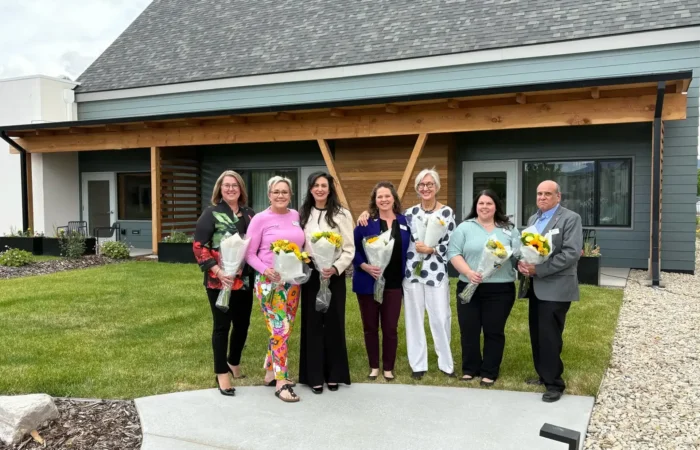 Secretary Christi Jacobsen: 'Surge in new business registrations continues across Montana' 2 Seven people stand in a row outside a modern Montana building, each holding a bouquet of yellow flowers and smiling at the camera. The group is dressed in business casual attire, perhaps celebrating recent business registrations.