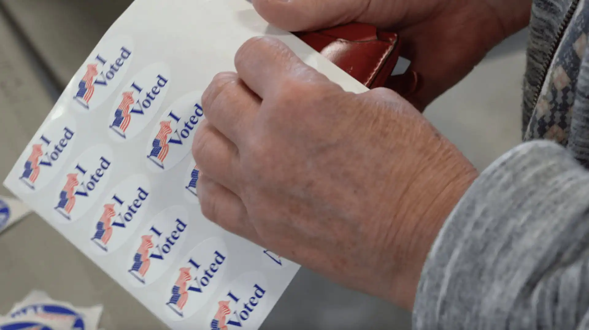 Montana Secretary of State Christi Jacobsen celebrates successful 2022 Primary Election 4 A person in a gray long-sleeve shirt peels off an I Voted sticker with an American flag, celebrating participation in the 2022 Primary Election overseen by Montana Secretary of State Christi Jacobsen.