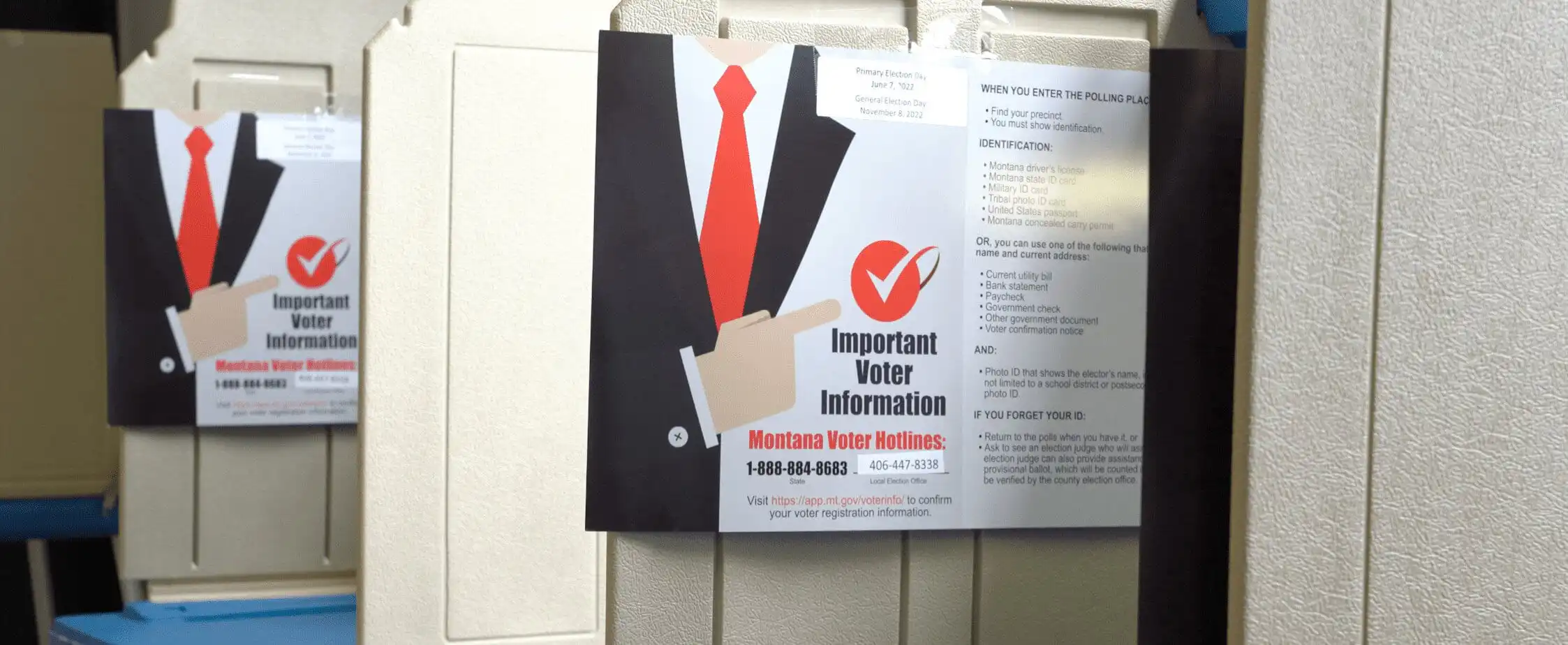 A voter information flyer highlighting the Secretary of States Office with a red tie graphic and a checkmark is attached to a beige voting booth. In the background, its reflection appears on another booth. The flyer mentions Montana voter information hotlines.