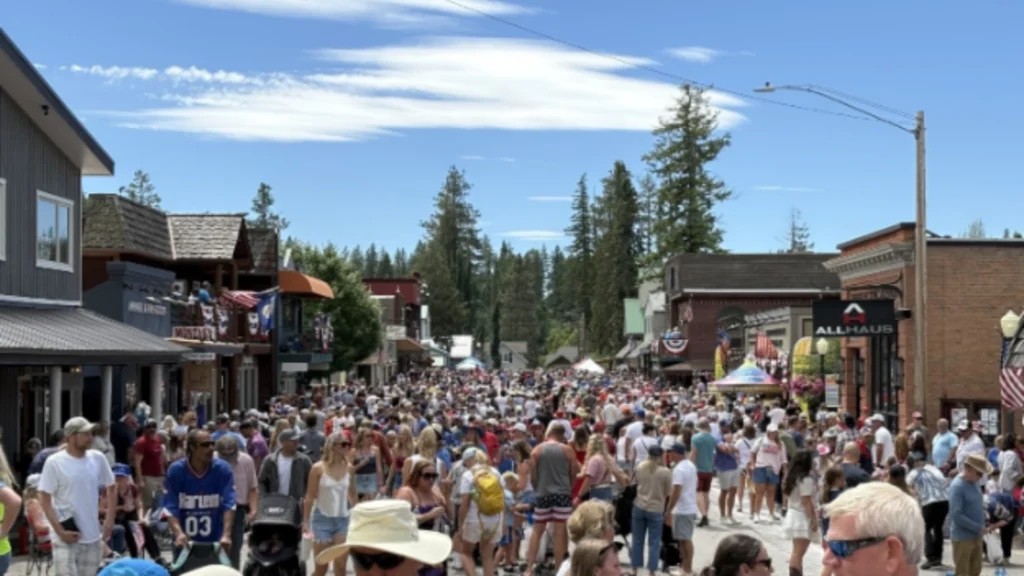 Christi Jacobsen - Montana Secretary of State 9 A large crowd of people fills a small town street during a sunny day, surrounded by shops and trees, with a blue sky overhead.