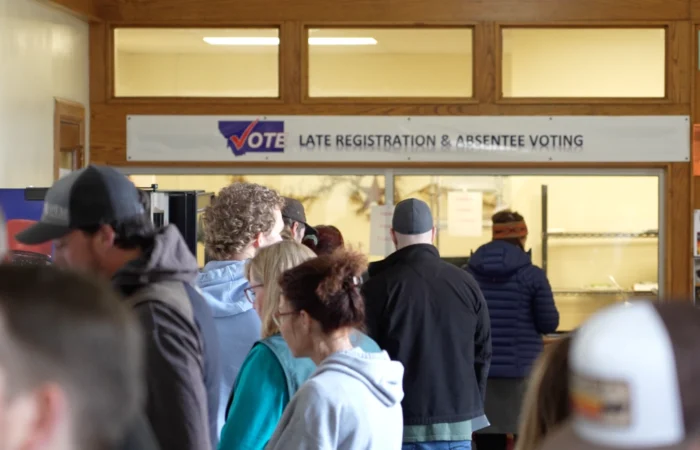 Montana election officials warn of increased potential for long lines on Election Day following court order 3 People stand in line at an indoor polling place near a sign that reads Vote - Late Registration & Absentee Voting, reflecting the busy atmosphere of the Montana Primary Election at local county election offices.