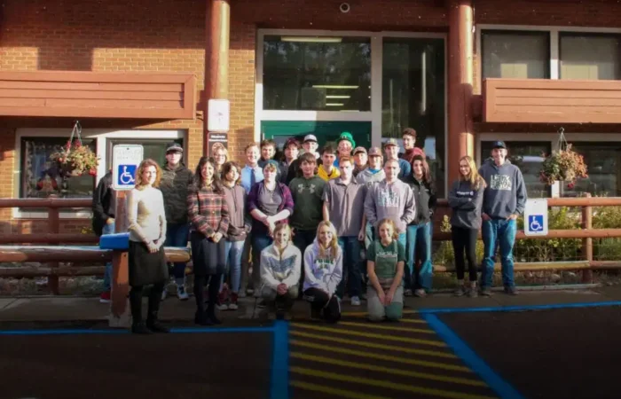 Secretary Jacobsen delivers 70 Constitutions to Lincoln High School 6 A large group of people pose for a photo outside Lincoln High School, a brick building with large windows. Some are standing, others kneeling in front, near accessible parking signs and hanging flower baskets. Secretary Jacobsen is also present.