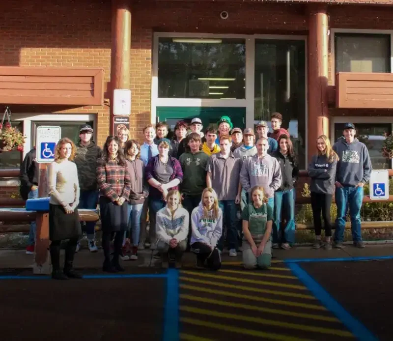 Secretary Jacobsen delivers 70 Constitutions to Lincoln High School 2 A large group of people pose for a photo outside Lincoln High School, a brick building with large windows. Some are standing, others kneeling in front, near accessible parking signs and hanging flower baskets. Secretary Jacobsen is also present.