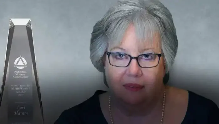 Montana Secretary of State Office's Lori Hamm honored with National Notary Association award 8 A woman with gray hair and glasses sits next to a tall, clear achievement award trophy against a gray background. The text on the trophy references Lori Hamm and the National Notary Association.