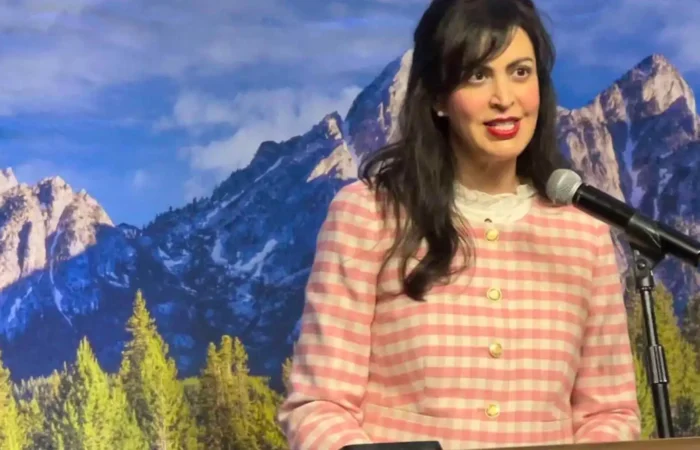 Secretary of State Christi Jacobsen: ‘New business registrations climb again in May’ 4 Christi Jacobsen, Montana Secretary of State, stands in a pink and white checkered jacket at a podium with a microphone, addressing new business registrations against a scenic backdrop of mountains and pine trees.