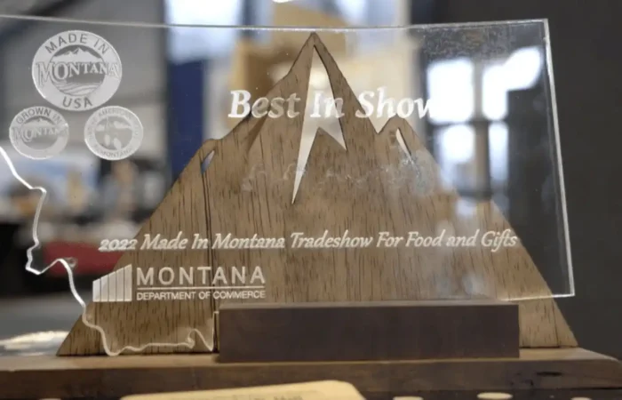Secretary Jacobsen congratulates 'Best in Show' winners at 2022 Made in Montana Tradeshow 8 A transparent award shaped like Montana with mountain outlines, etched with Best in Show, 2022 Made in Montana Tradeshow For Food and Gifts, Montana Department of Commerce.