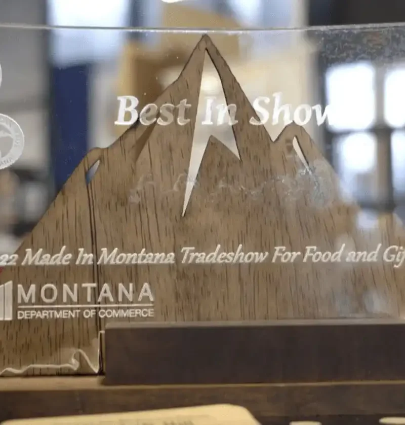 A transparent award shaped like Montana with mountain outlines, etched with Best in Show, 2022 Made in Montana Tradeshow For Food and Gifts, Montana Department of Commerce.