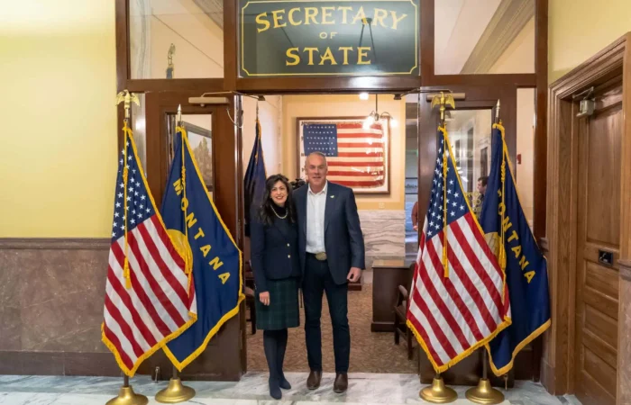 Secretary of State’s Office processes 25 candidate filings Friday; 203 filings to date 9 Two people stand smiling under a Secretary of State sign, surrounded by Montana and U.S. flags in an official-looking building with marble floors—possibly celebrating recent candidate filings—with an American flag in the background.