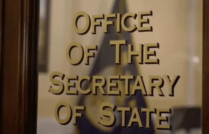 Montana's 2022 candidate filing entering final week 3 Glass door with gold lettering that reads Office Of The Secretary Of State, referencing Montana elections, with a blurred flag and interior visible in the background.