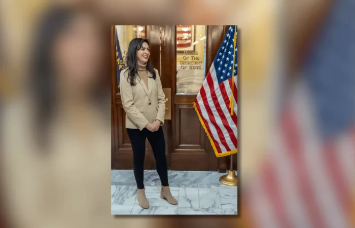 Secretary of State Christi Jacobsen announces new business registrations continued climbing in July 1 A woman stands indoors near a wooden door labeled Office of the Secretary of State. Smiling, she wears a tan blazer, black pants, and tan boots. An American flag is to her right, highlighting Christi Jacobsen’s role in new business registrations.