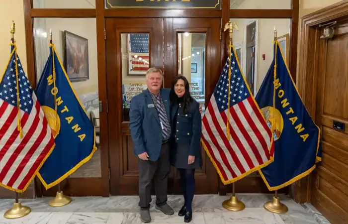 From the classroom to the Capitol — Secretary Christi Jacobsen celebrates longtime Montana teacher Bob Tipton 5 Christi Jacobsen and Bob Tipton stand side by side in front of a wooden door, flanked by U.S. flags and Montana state flags, in a formal indoor setting with marble floors—celebrating the achievements of a dedicated Montana teacher.